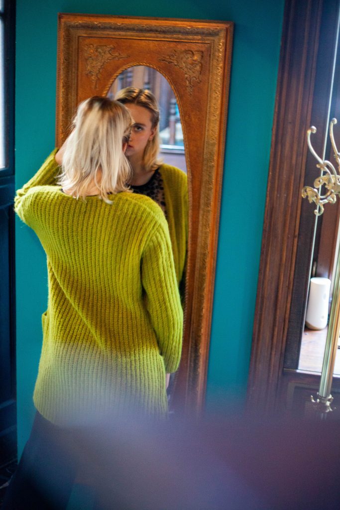 Blonde Frau in olivgrünem Strick-Cardigan schaut in einen goldenen Spiegel, Fashion-Porträt von Bonner Fotografin
