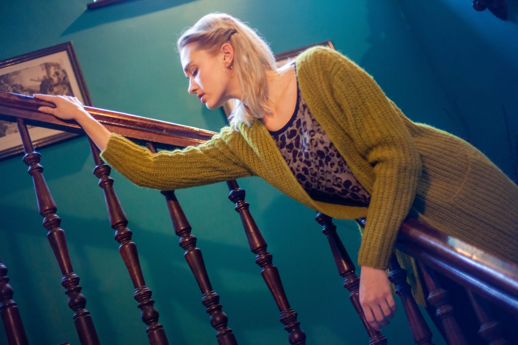 Modell im olivgrünen Cardigan auf dunkler Holztreppe, professionell fotografiert für Fashion Blog von Malin Kalwa