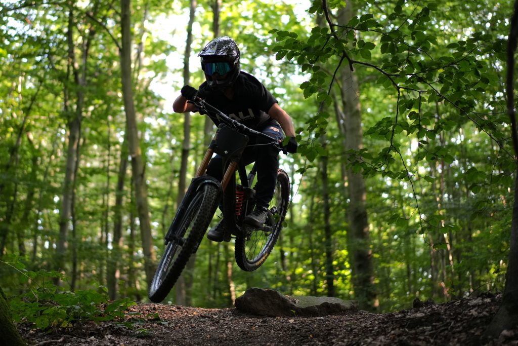 Mountainbiker im Downhill-Look springt über Wurzel im Wald, ideales Foto für MTB Social Media Kampagne von Fotografin Bonn