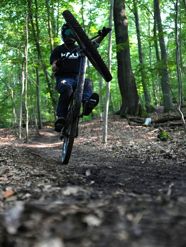 MTB-Fahrer im Kali Protectives Shirt balanciert auf Hinterrad (Manual/Wheelie) auf Waldtrail, professionelles Foto von Malin Kalwa